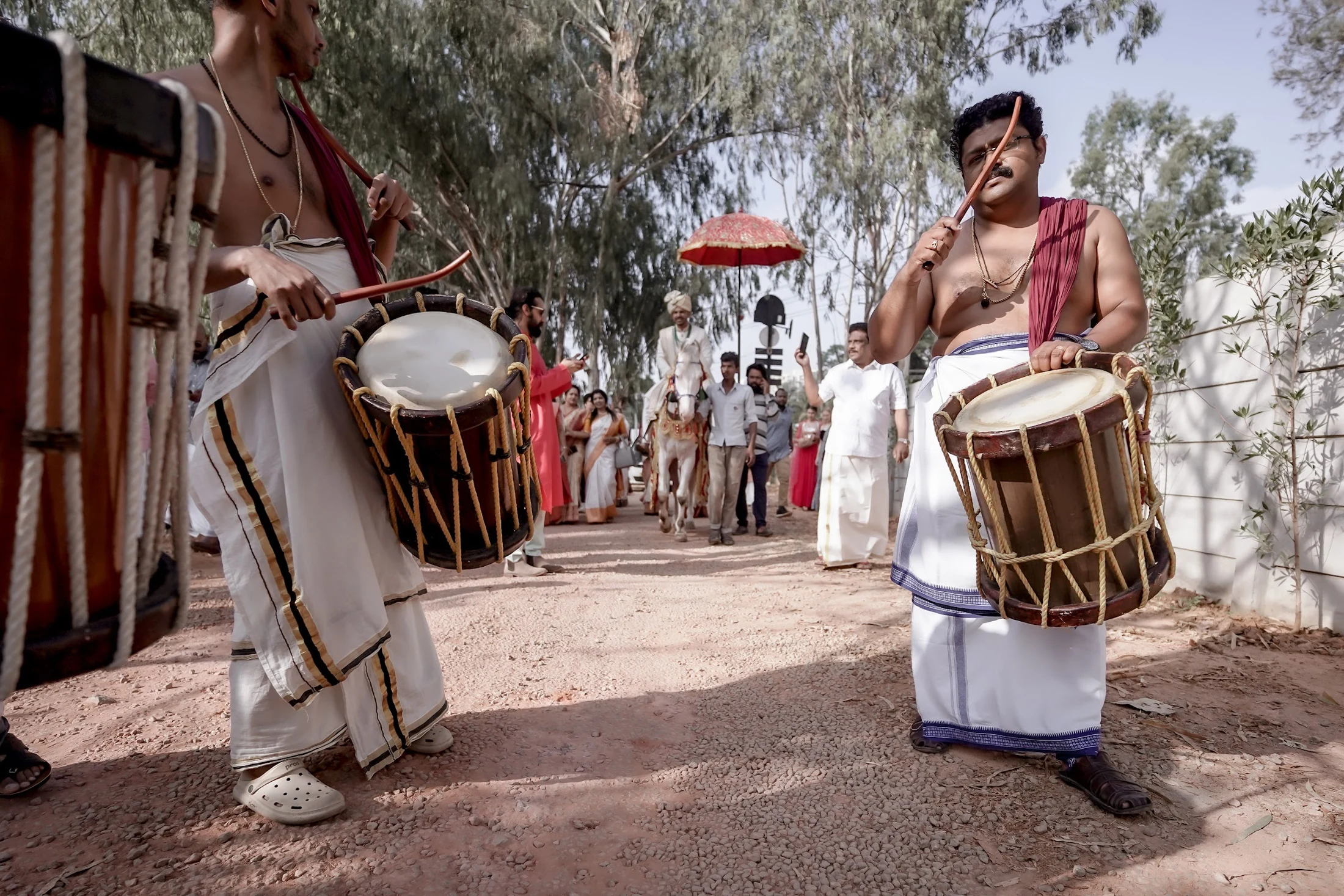 Traditional drummers leading the groom and wedding guests along an outdoor arrival route.