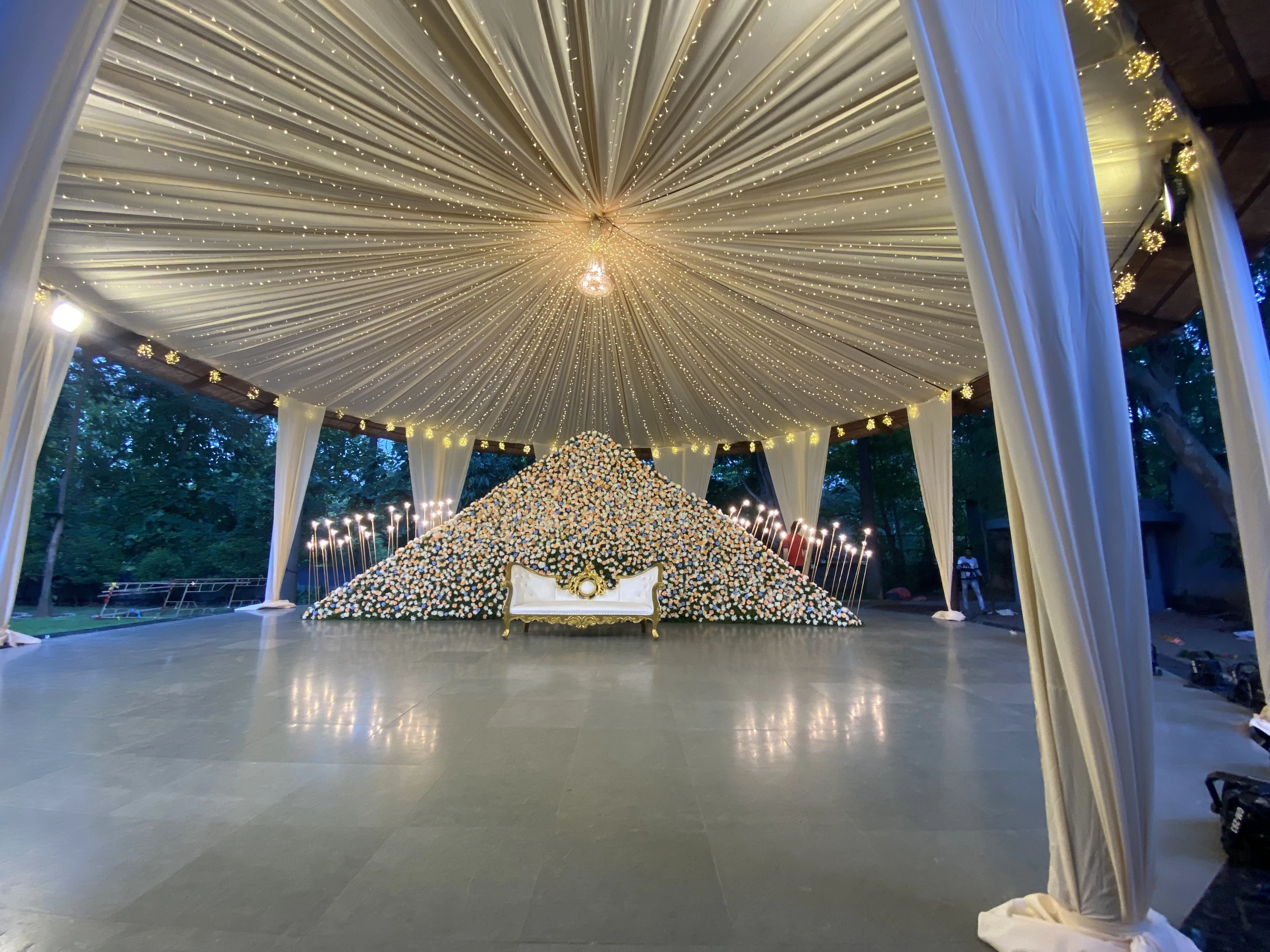 A floral reception stage beneath an illuminated pleated canopy