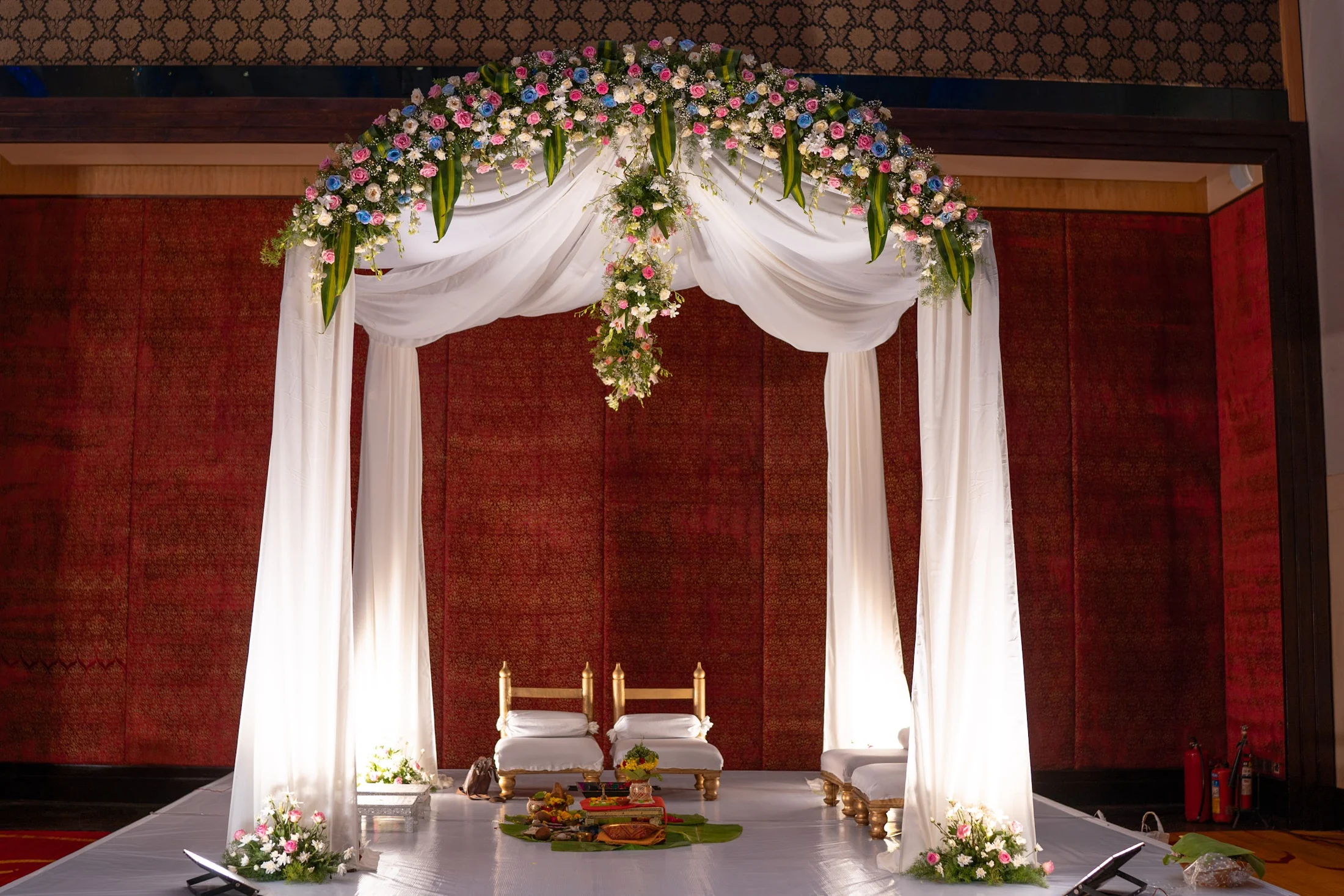 A ceremony mandap with drapes, flowers and brass vessels