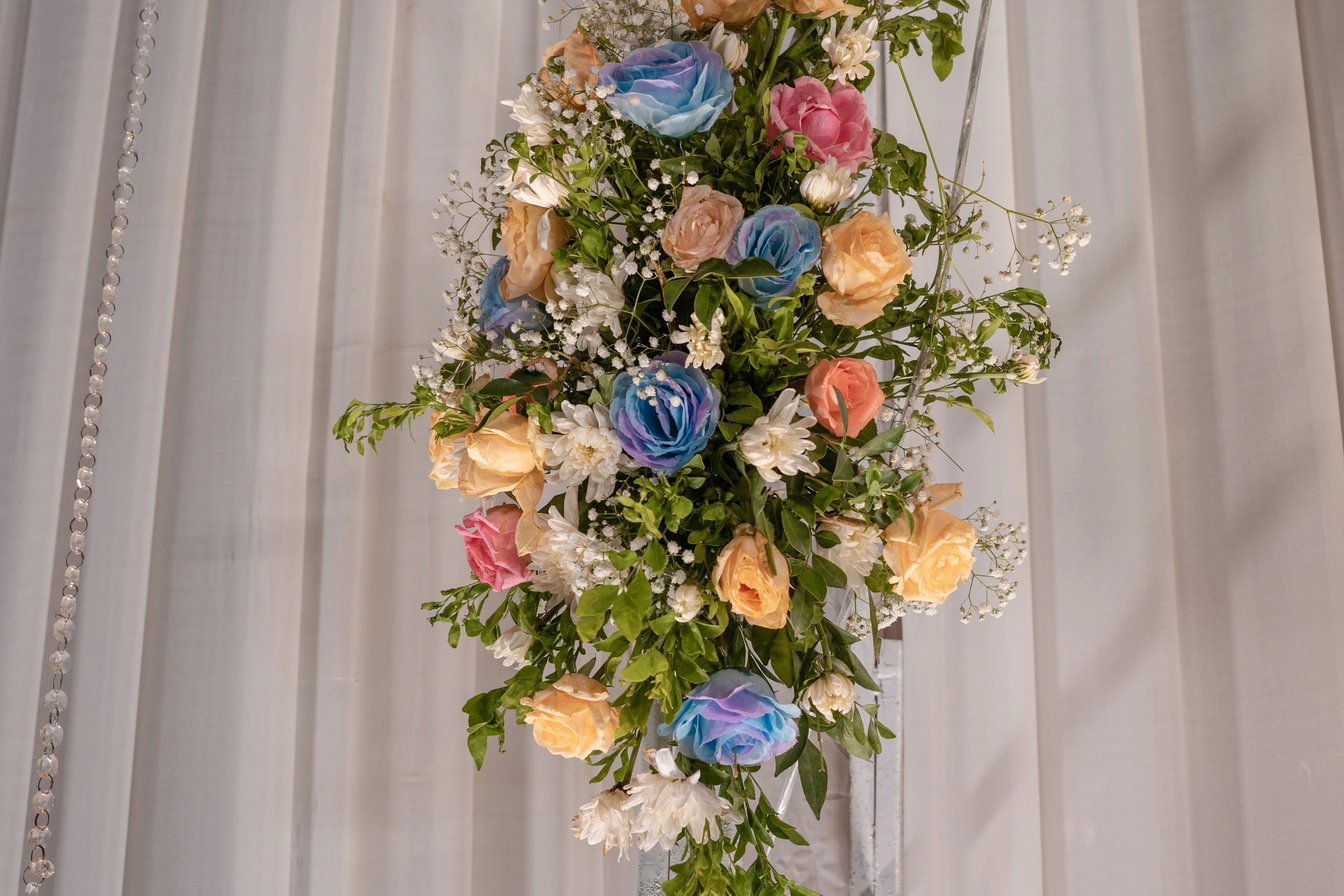 Peach, pink, white and blue flowers arranged on a draped floral column.
