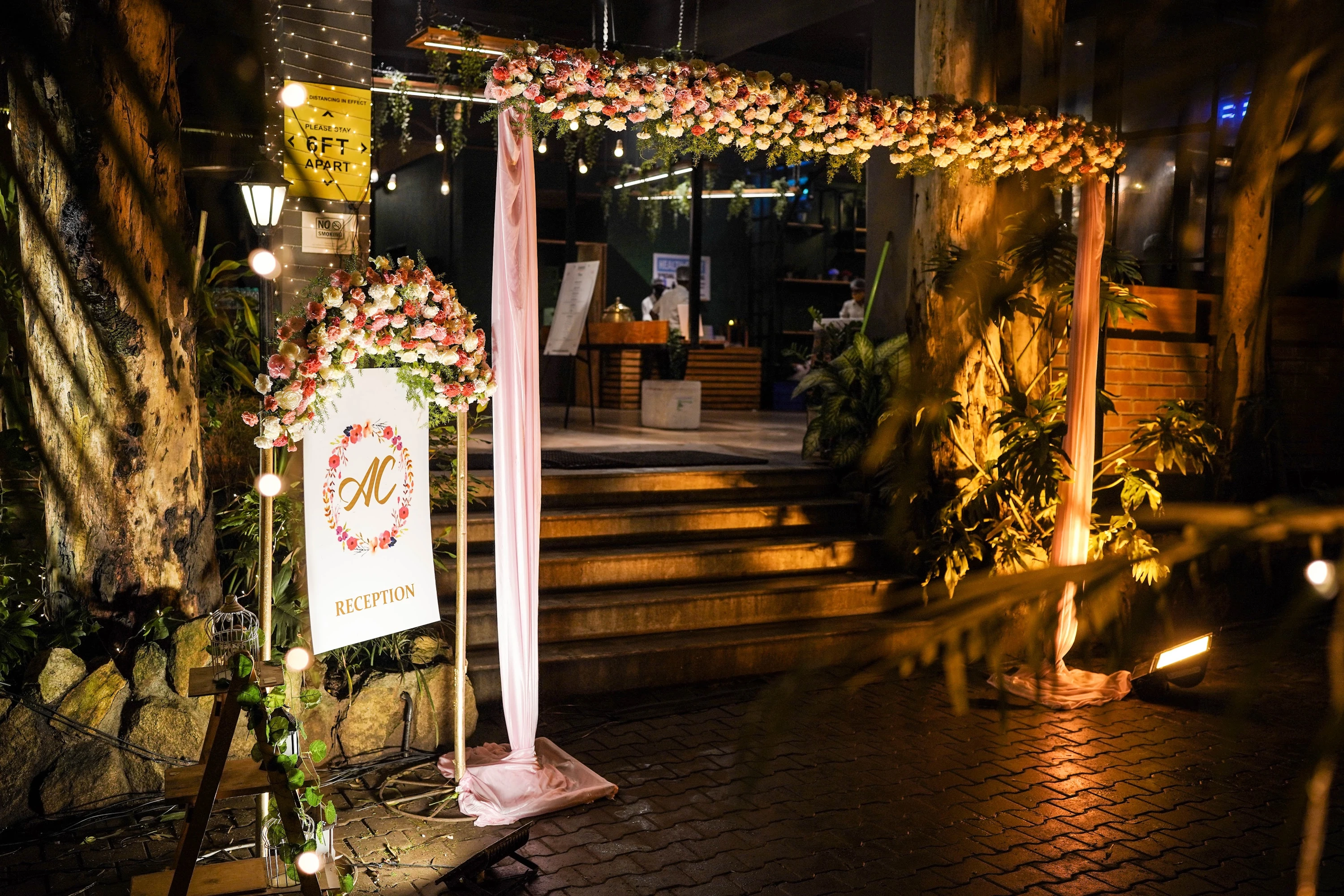 A warm illuminated wedding arrival arch with flowers and hanging lights