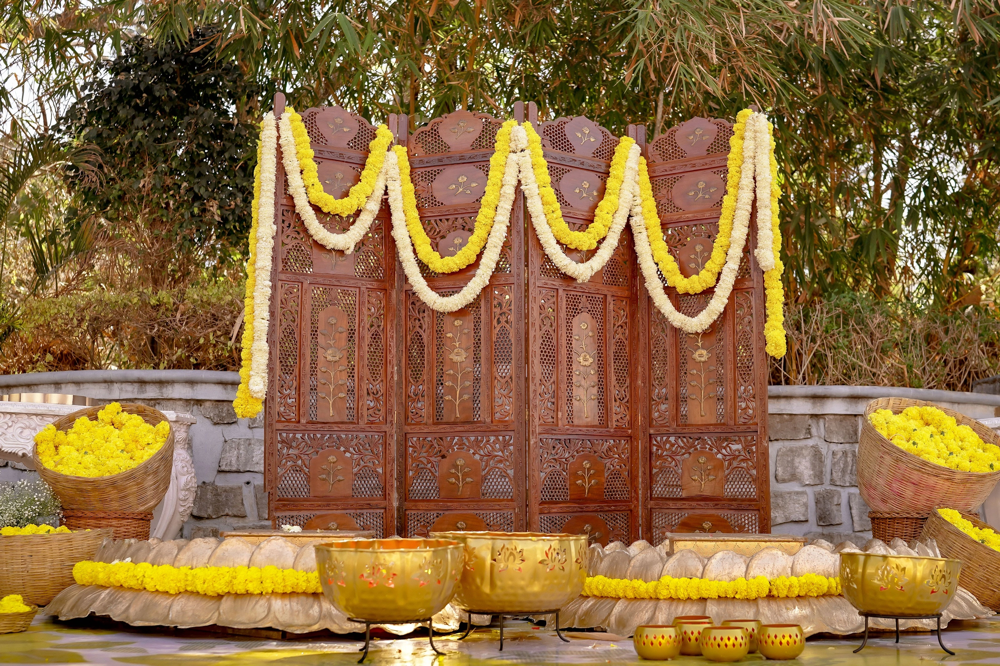 A carved wooden backdrop styled with yellow flowers and haldi baskets