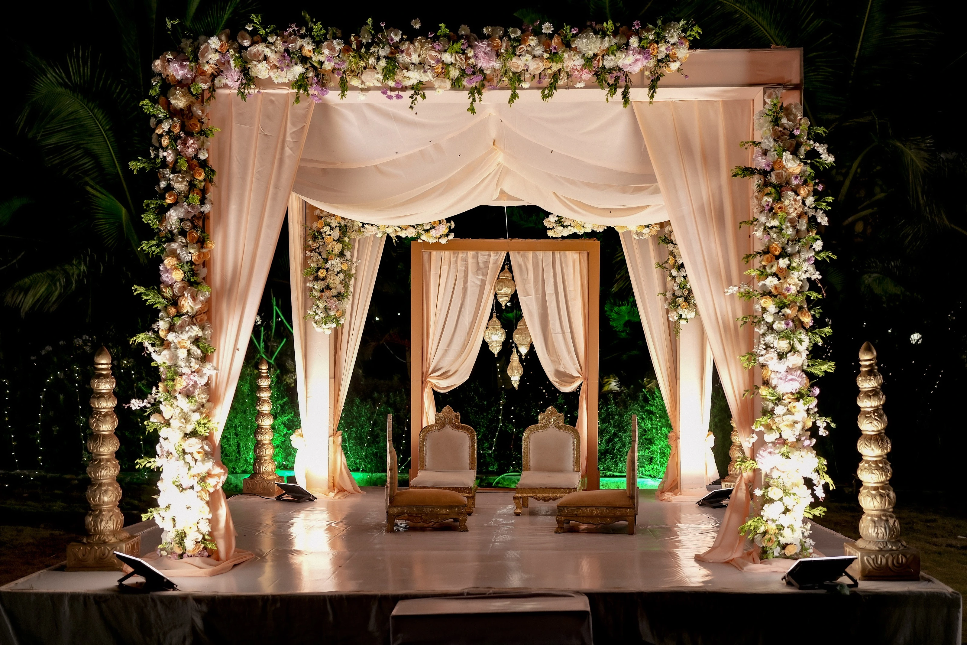 A warmly lit evening mandap approached through flower-framed drapes