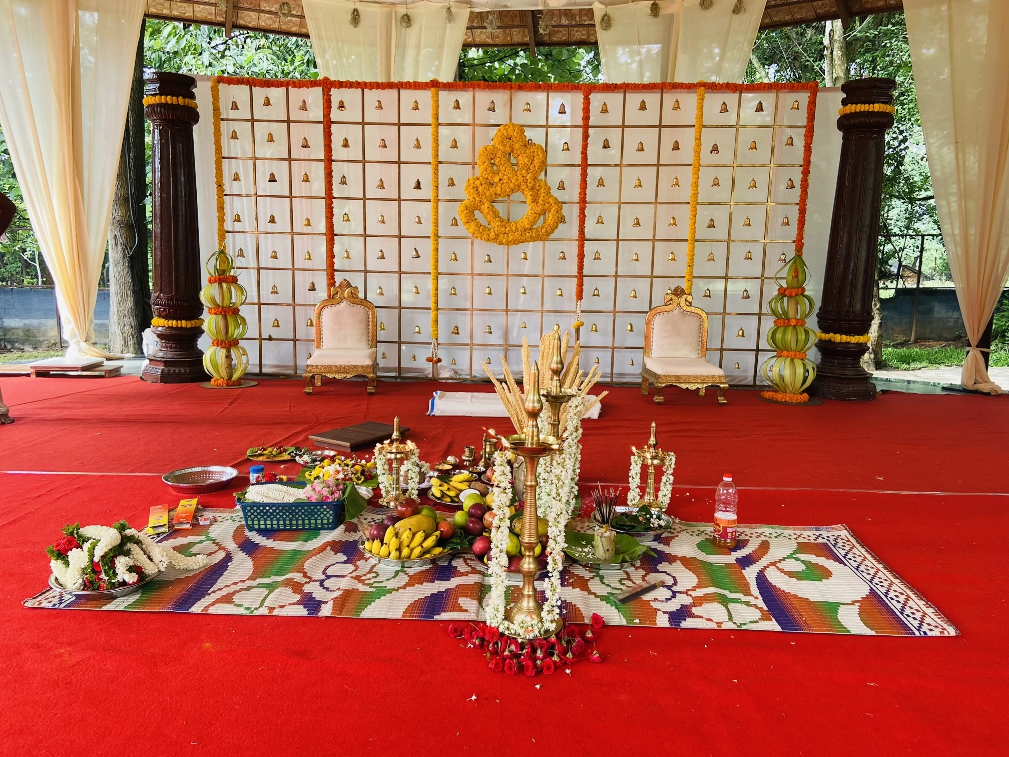 A ceremony setting with brass lamps, offerings, marigold details and a red-carpeted pavilion