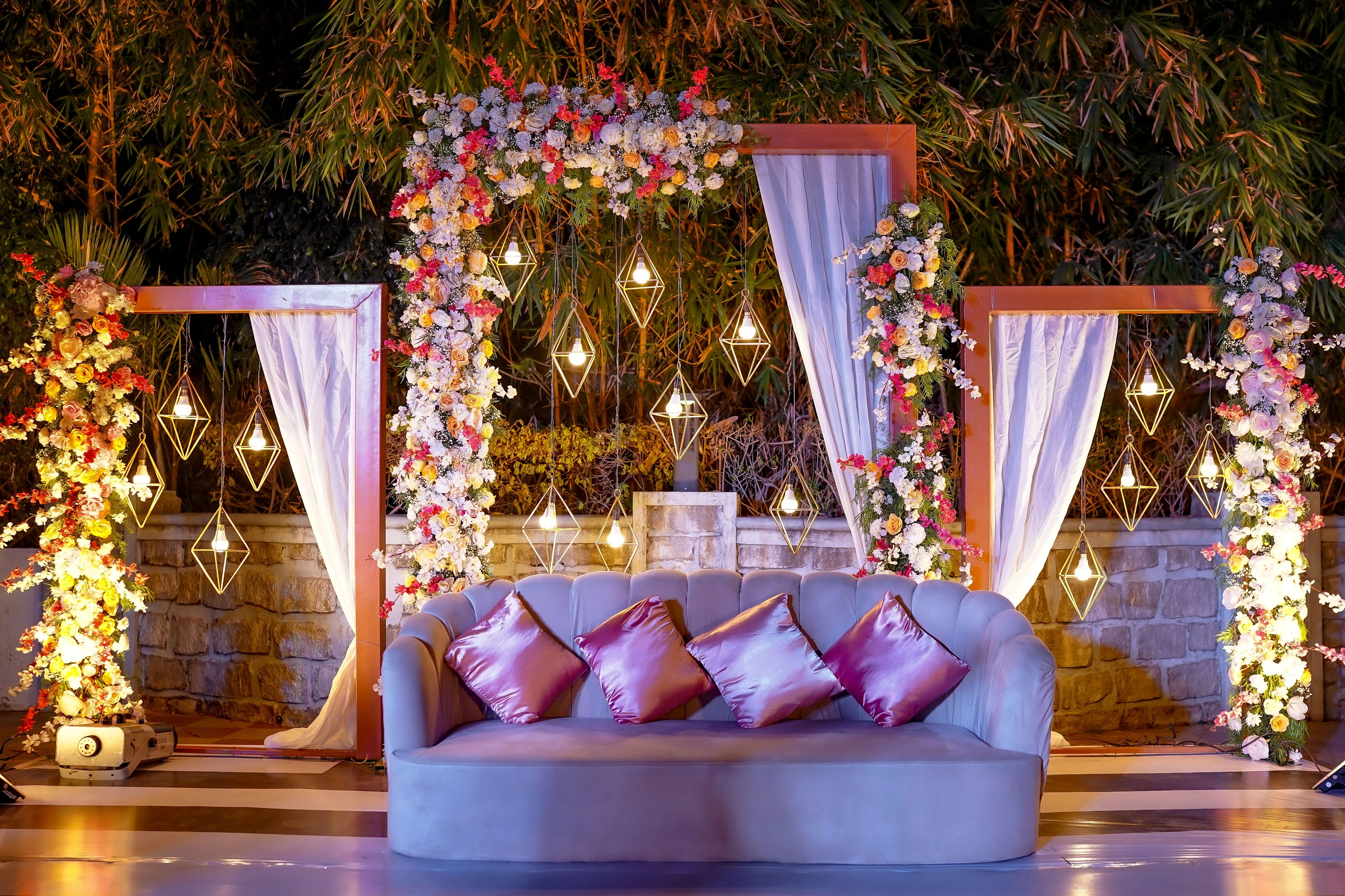 A violet reception sofa framed by flowers, drapes and geometric lights