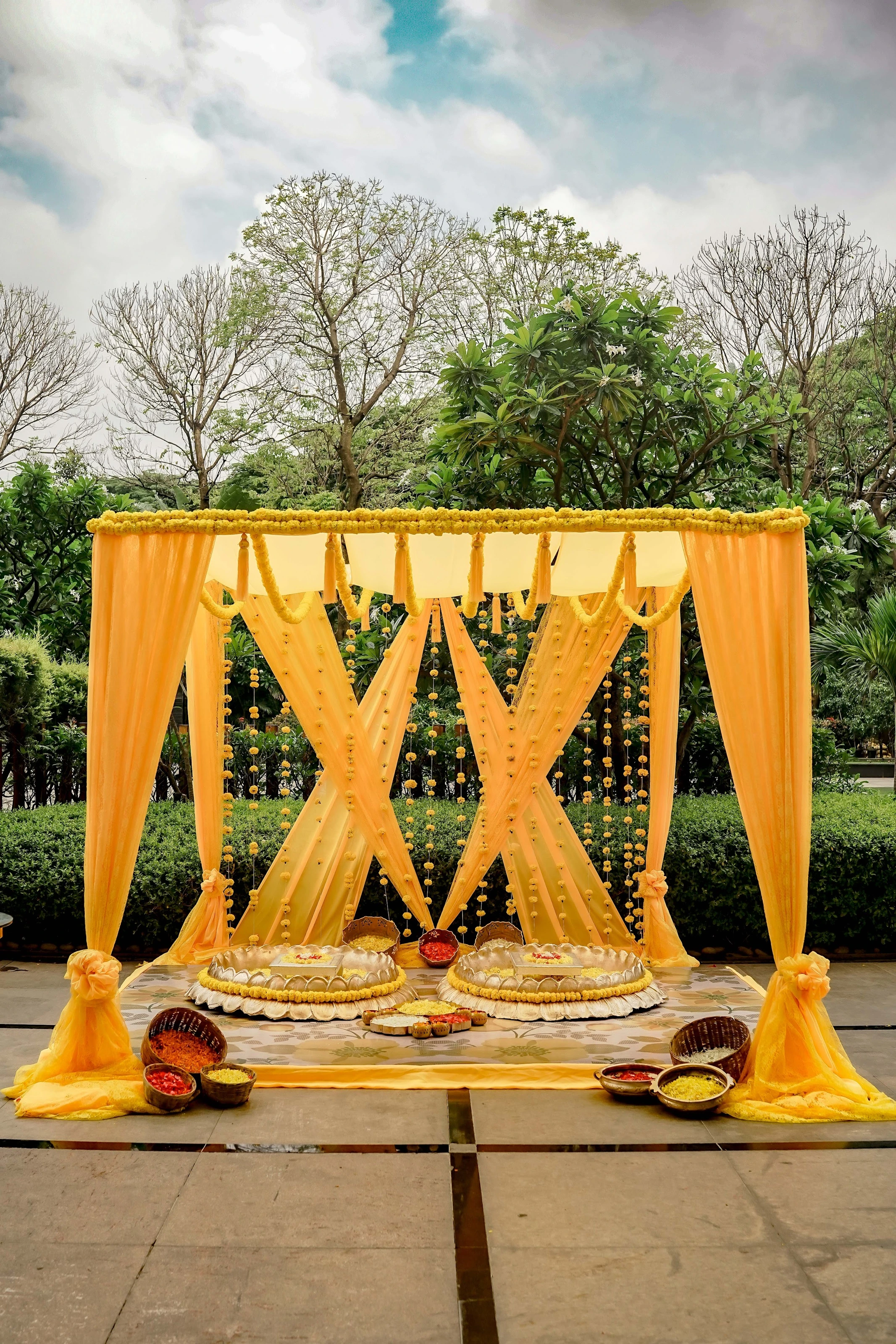 A yellow haldi canopy with seats, flower baskets and a petal-shower station