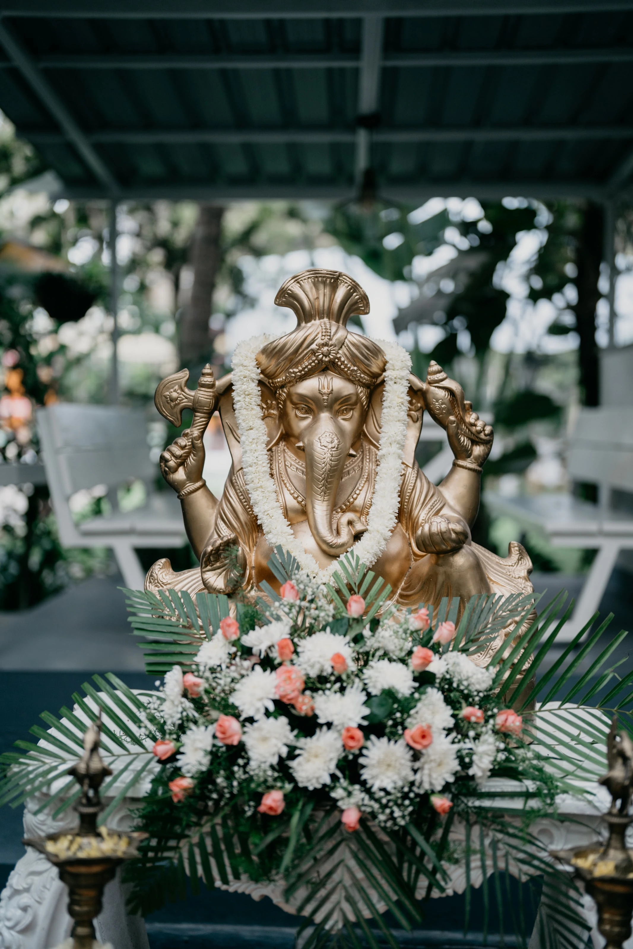 A Ganesh statue surrounded by flowers, greenery and brass lamps