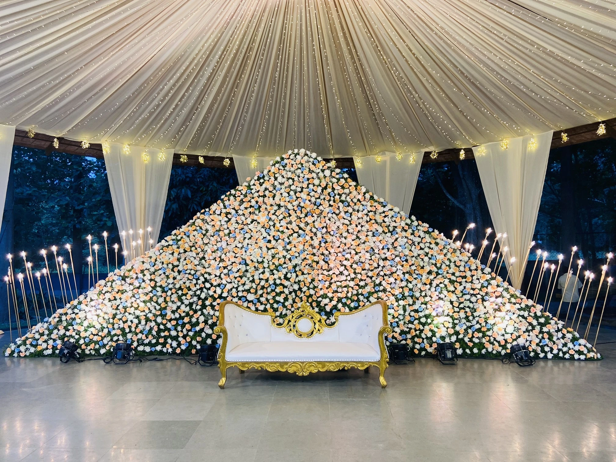A sweeping ivory floral reception stage beneath a pleated canopy