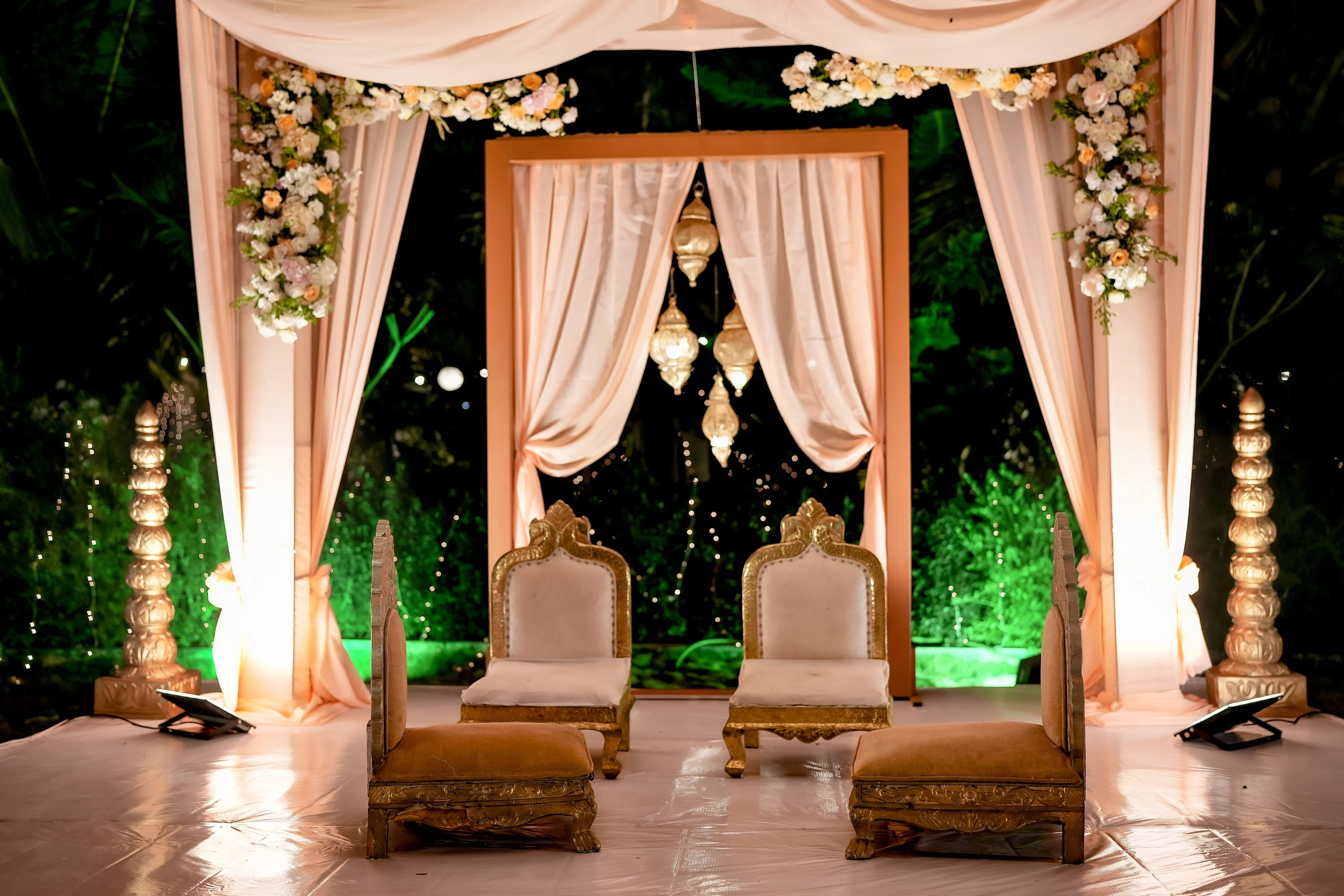 An evening ceremony mandap with warm drapes, flowers and carved chairs