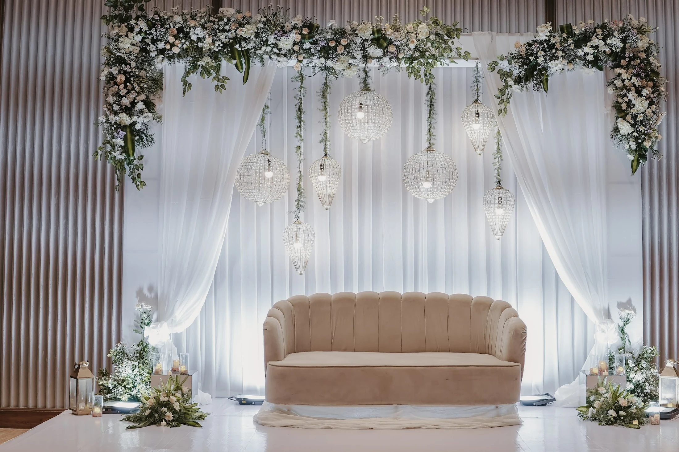 White drapes, suspended lights and fresh flowers framing an ivory reception sofa.